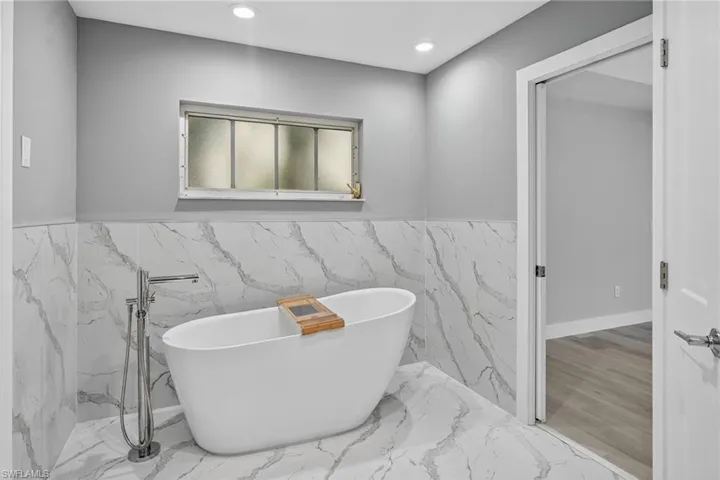 Bathroom featuring a soaking tub, tile walls, tiled flooring and recessed lighting.