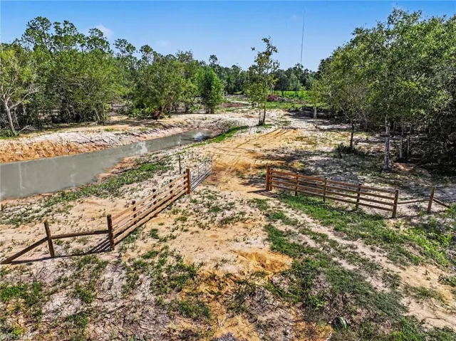 Expansive land parcel featuring a pond and wooden fencing at the entry, and established trees