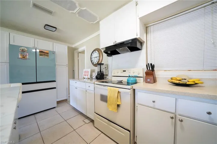 Kitchen with visible vents, under cabinet range hood, light tile patterned floors, freestanding refrigerator, and white electric range oven
