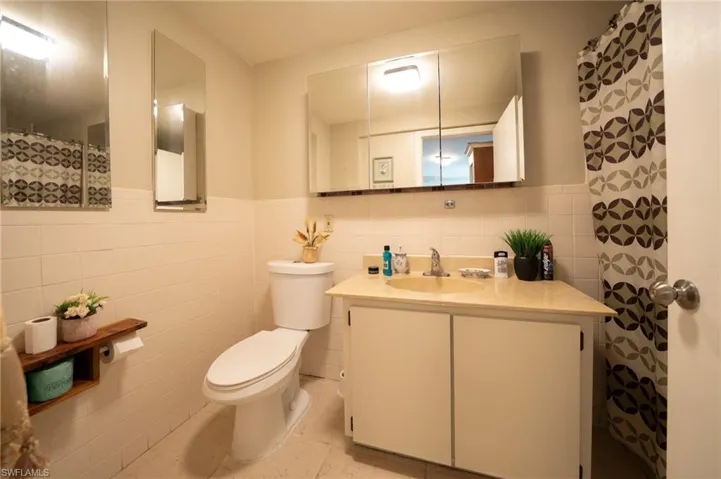 Full bathroom featuring tile walls, wainscoting, toilet, and vanity