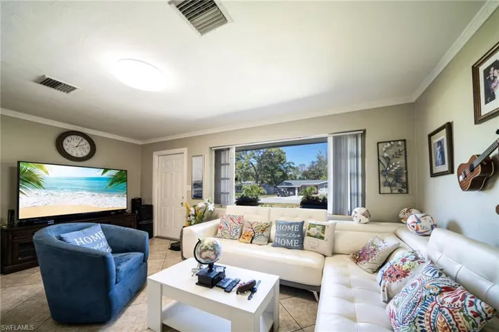 Living area featuring tile patterned floors, visible vents, and crown molding