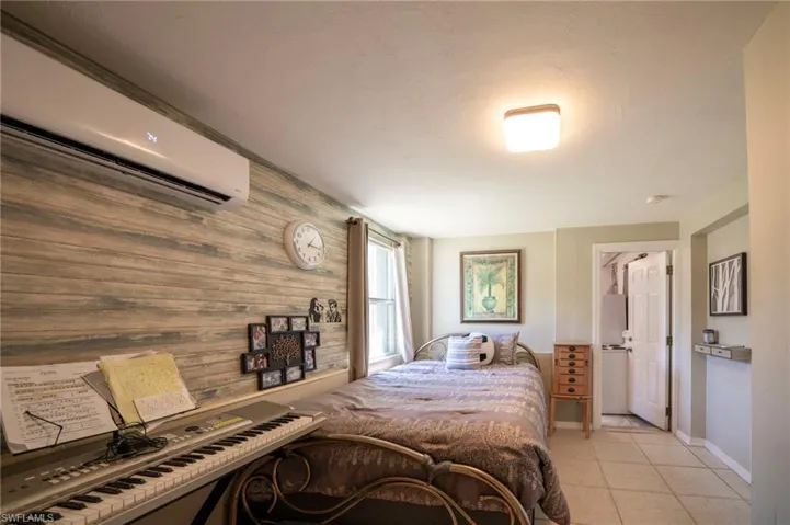 Bedroom with light tile patterned flooring, wood walls, an AC wall unit, and baseboards