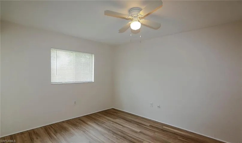 Wood-finish flooring, white walls, single window with blinds, and a ceiling fan with integrated lighting