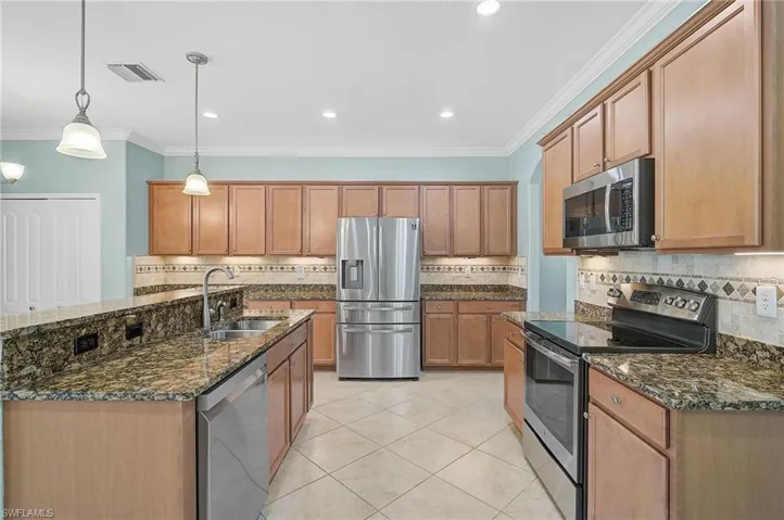 Kitchen with appliances with stainless steel finishes, hanging light fixtures, dark stone counters, ornamental molding, and sink