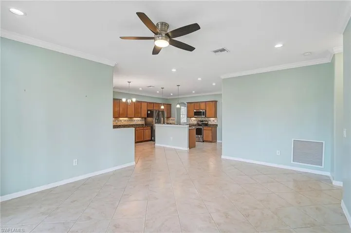 Unfurnished family room featuring ceiling fan with notable chandelier, ornamental molding, and light tile patterned floors