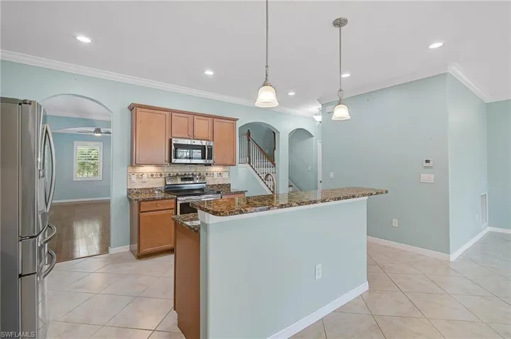 Kitchen with dark stone countertops, stainless steel appliances, crown molding, light tile patterned floors, and pendant lighting