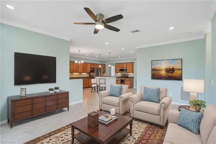 Tiled living room with ceiling fan with notable chandelier and ornamental molding