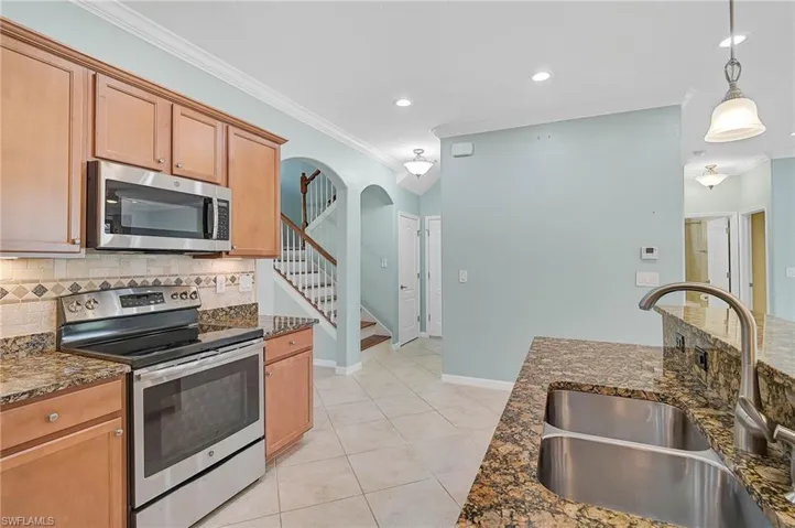 Kitchen featuring stainless steel appliances, decorative backsplash, crown molding, dark stone counters, and sink