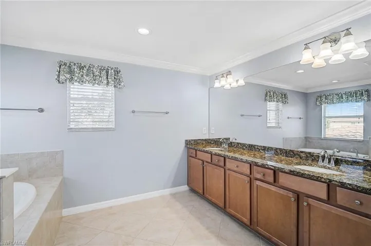 Bathroom featuring vanity, tile patterned floors, ornamental molding, and tiled tub