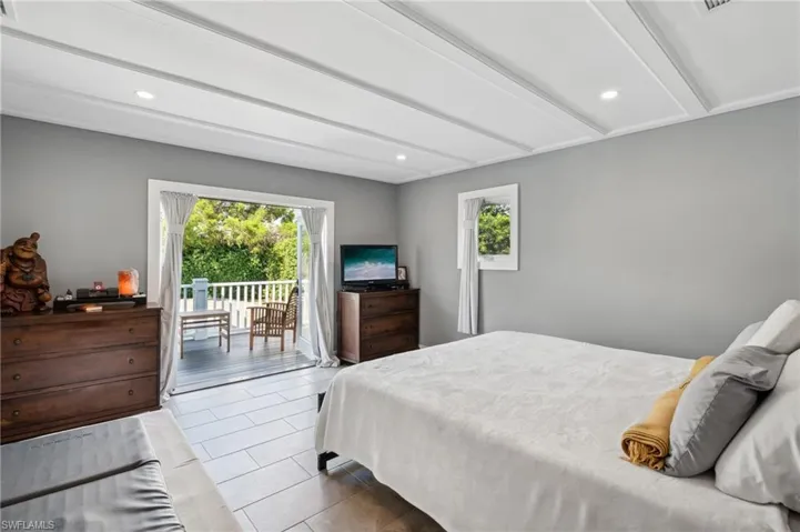 Tiled bedroom with beamed ceiling and access to exterior