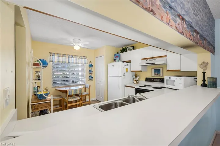 Kitchen featuring light countertops, range with electric cooktop, white cabinetry, freestanding refrigerator, and ceiling fan