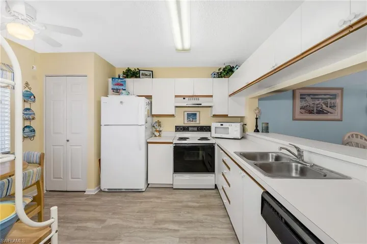 Kitchen with white cabinets, white appliances, light countertops, light wood-style flooring, and a textured ceiling