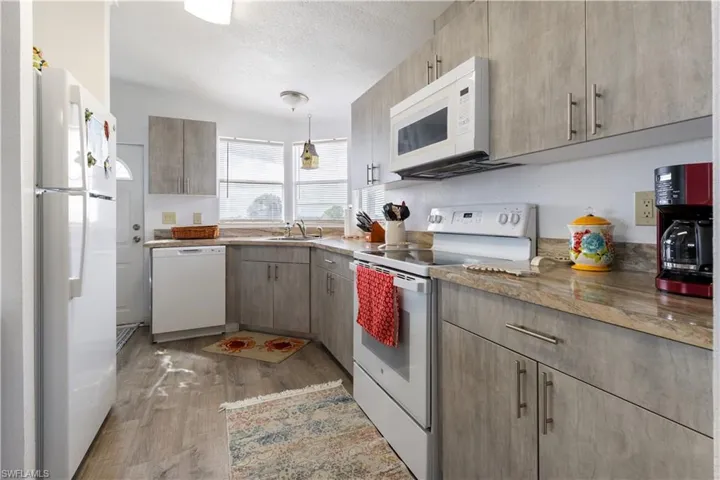 Kitchen featuring white appliances, a textured ceiling, light wood-style flooring, and decorative light fixtures
