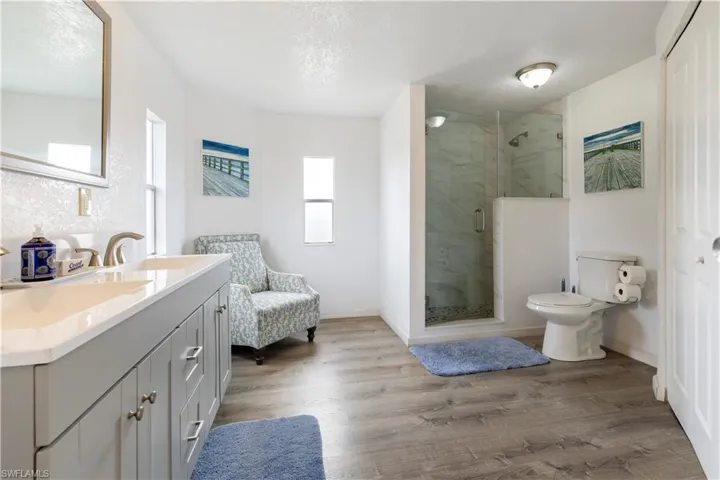 Bathroom with double vanity, a marble finish shower, light wood-style flooring, and a textured ceiling