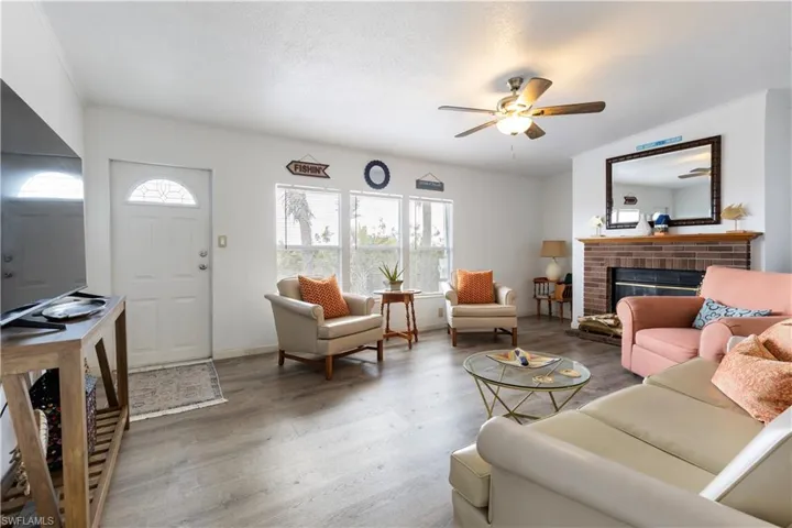 Living area featuring a ceiling fan, a brick fireplace, wood finished floors, and crown molding