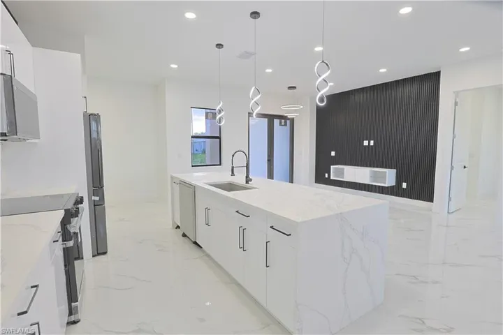Kitchen featuring light marble finish floors, modern cabinets, stainless steel appliances, recessed lighting, and a large island