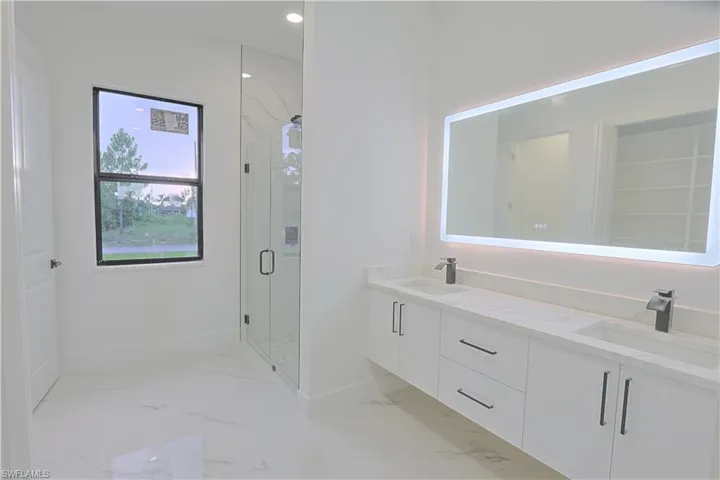 Bathroom featuring marble look tile flooring, a marble finish shower, double vanity, and recessed lighting