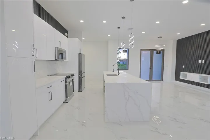Kitchen featuring stainless steel appliances, modern cabinets, recessed lighting, white cabinetry, and light marble finish floors