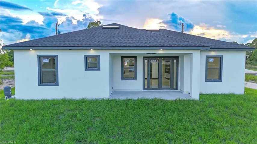 Back of property at dusk with a shingled roof, a lawn, and stucco siding