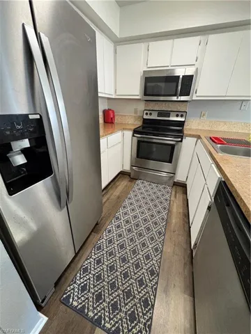 Kitchen featuring stainless steel appliances, white cabinets, and dark wood-type flooring