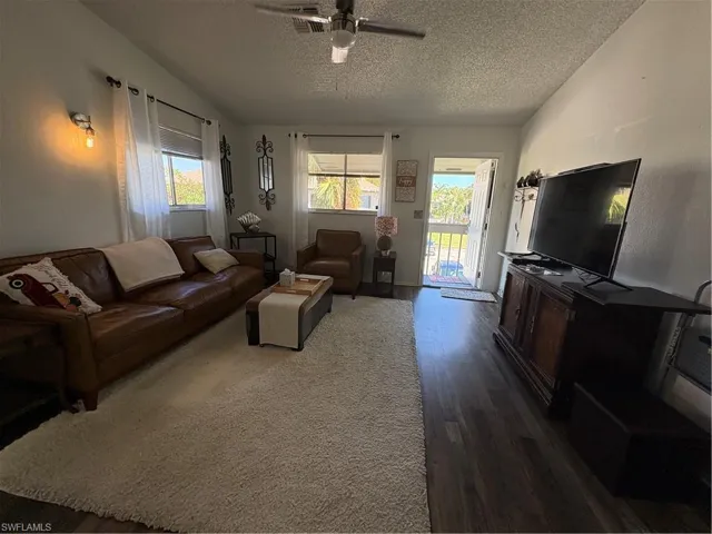 Living room with dark wood-type flooring, a ceiling fan, and a textured ceiling