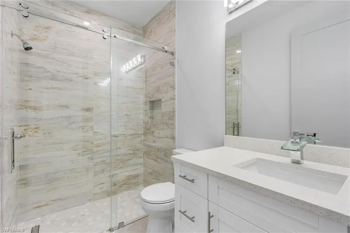 Contemporary bathroom featuring a frameless glass shower enclosure with a rain showerhead, a built-in shower niche, and large format natural stone-look wall tiles