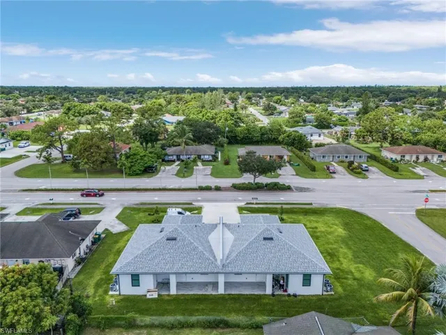 Duplex property featuring a light gray shingle roof, white exterior siding, covered parking, and an expansive green lawn