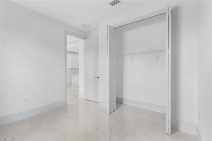 Room featuring light-toned large format tile flooring, white painted walls, and a bi-fold closet with shelving
