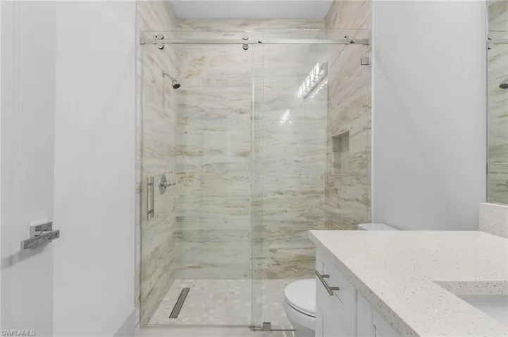 Walk-in shower featuring a frameless glass enclosure, natural stone-finish wall tile, hexagonal floor tile, and a built-in shower niche