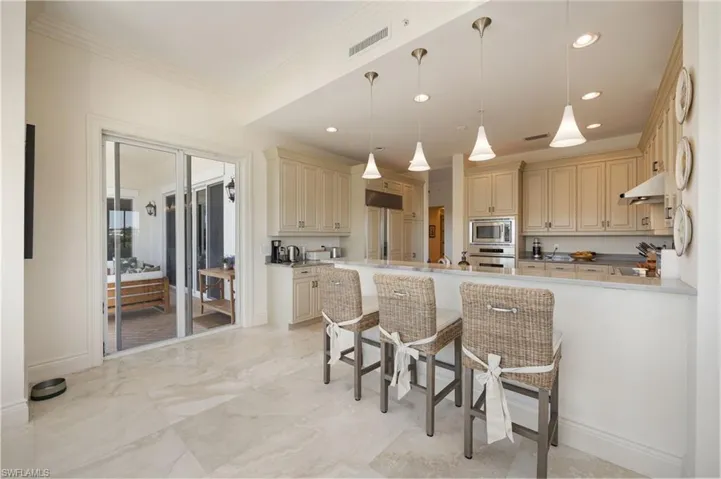 Kitchen with cream cabinets, decorative light fixtures, a kitchen breakfast bar, a peninsula, and built in appliances
