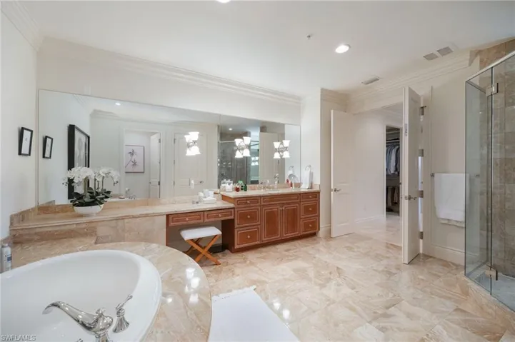 Full bathroom with vanity, a shower stall, a walk in closet, a garden tub, and crown molding
