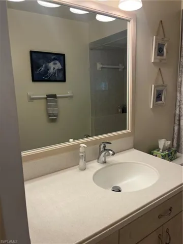 Bathroom vanity featuring an integrated sink with a chrome faucet, light-toned countertop, and a framed mirror with overhead lighting