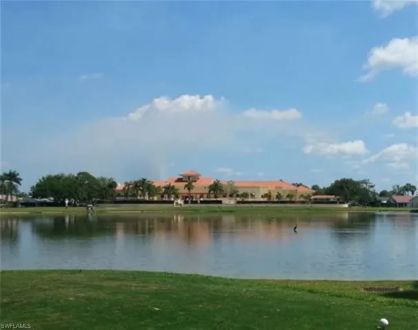Waterfront property featuring a large structure with a terra cotta roof and surrounding palm trees