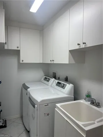 Laundry room featuring white cabinetry with silver-toned hardware, a utility sink with a chrome faucet, and tile flooring