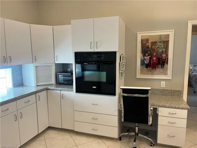 Kitchen workspace featuring white cabinetry, a built-in oven, granite-finish countertops, and tile flooring