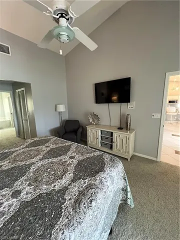 Vaulted ceiling with a ceiling fan, light gray wall paint, and gray carpet flooring
