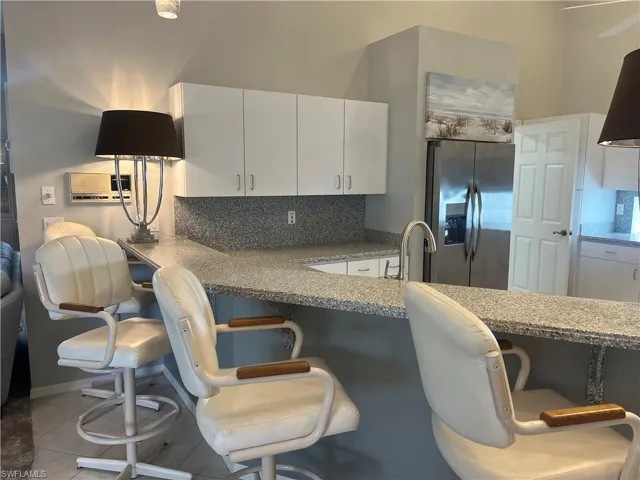 Kitchen featuring white upper cabinetry, stainless steel refrigerator, and a large breakfast bar with solid surface countertops and integrated sink