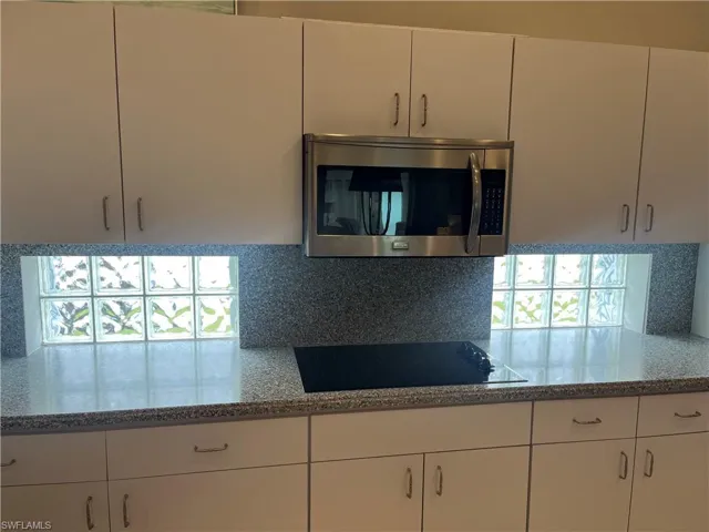 Kitchen featuring white cabinetry, an integrated cooktop, a stainless steel over-the-range microwave, speckled countertops, and a glass block window