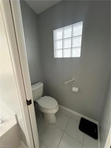 Bathroom featuring a glass block window, light gray walls, white tile flooring, and a white toilet