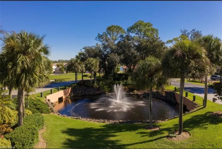 Lush landscaping featuring a pond with a fountain, surrounded by palm trees and mature foliage, alongside paved pathways