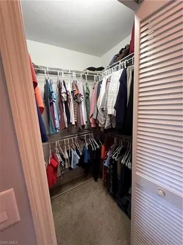Walk-in closet featuring wire shelving, multiple hanging rods, wall-to-wall carpeting, and a louvered bi-fold door