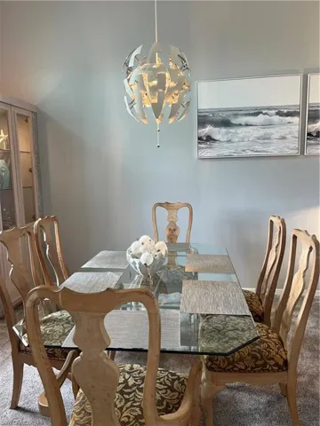 Dining area featuring a geometric pendant light fixture, glass-top dining table, patterned upholstered chairs, and light gray wall paint