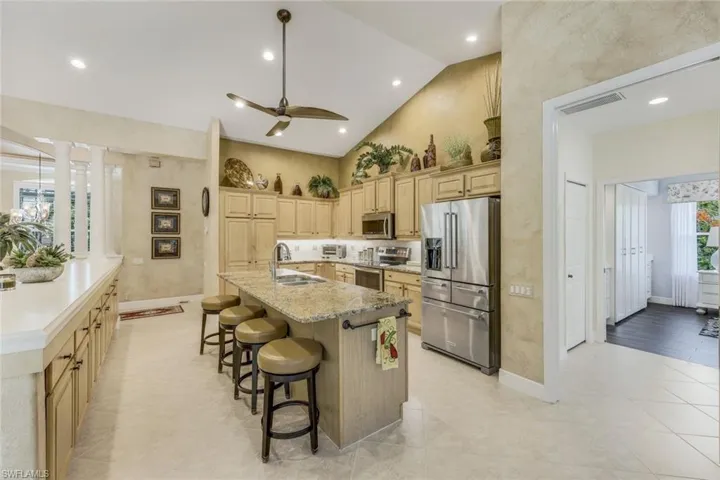 Kitchen featuring a center island with sink, appliances with stainless steel finishes, a breakfast bar area, high vaulted ceiling, and ceiling fan.