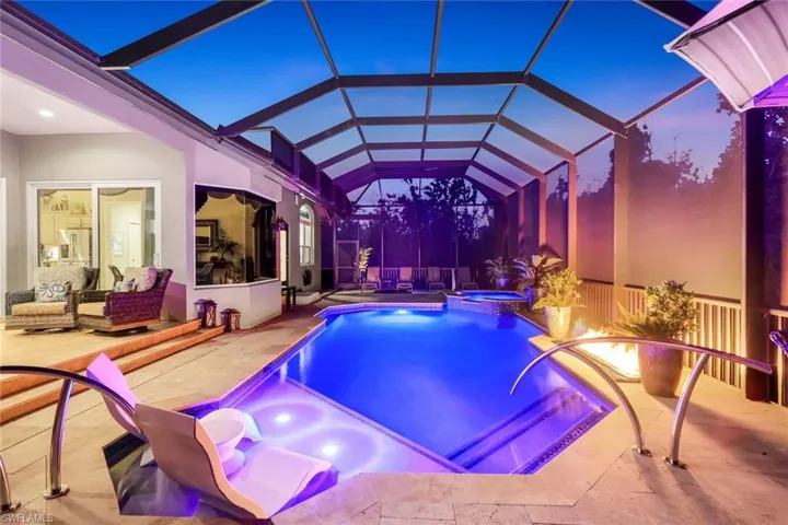 Pool at dusk featuring an in ground hot tub, a patio, and a lanai