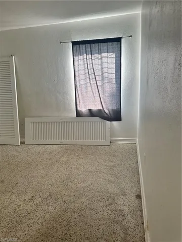 Unfurnished room with a textured wall, baseboards, and speckled floor