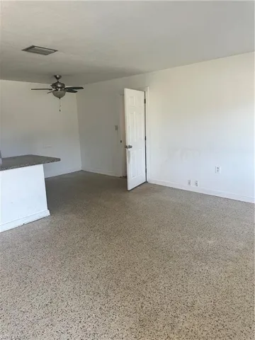 Empty room featuring baseboards, visible vents, ceiling fan, and speckled floor