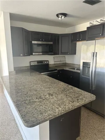 Kitchen featuring refrigerator, range, a sink, stone counters, and a peninsula