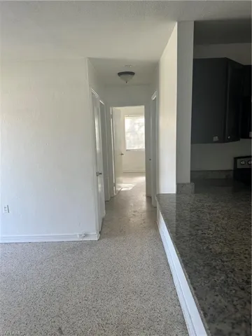 Hall featuring baseboards, a textured ceiling, a textured wall, and light speckled floor