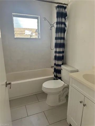 Bathroom featuring toilet, shower / tub combo with curtain, vanity, and tile patterned flooring