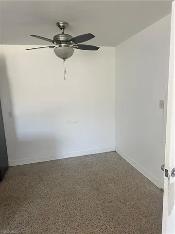 Empty room with a ceiling fan, speckled floor, and baseboards